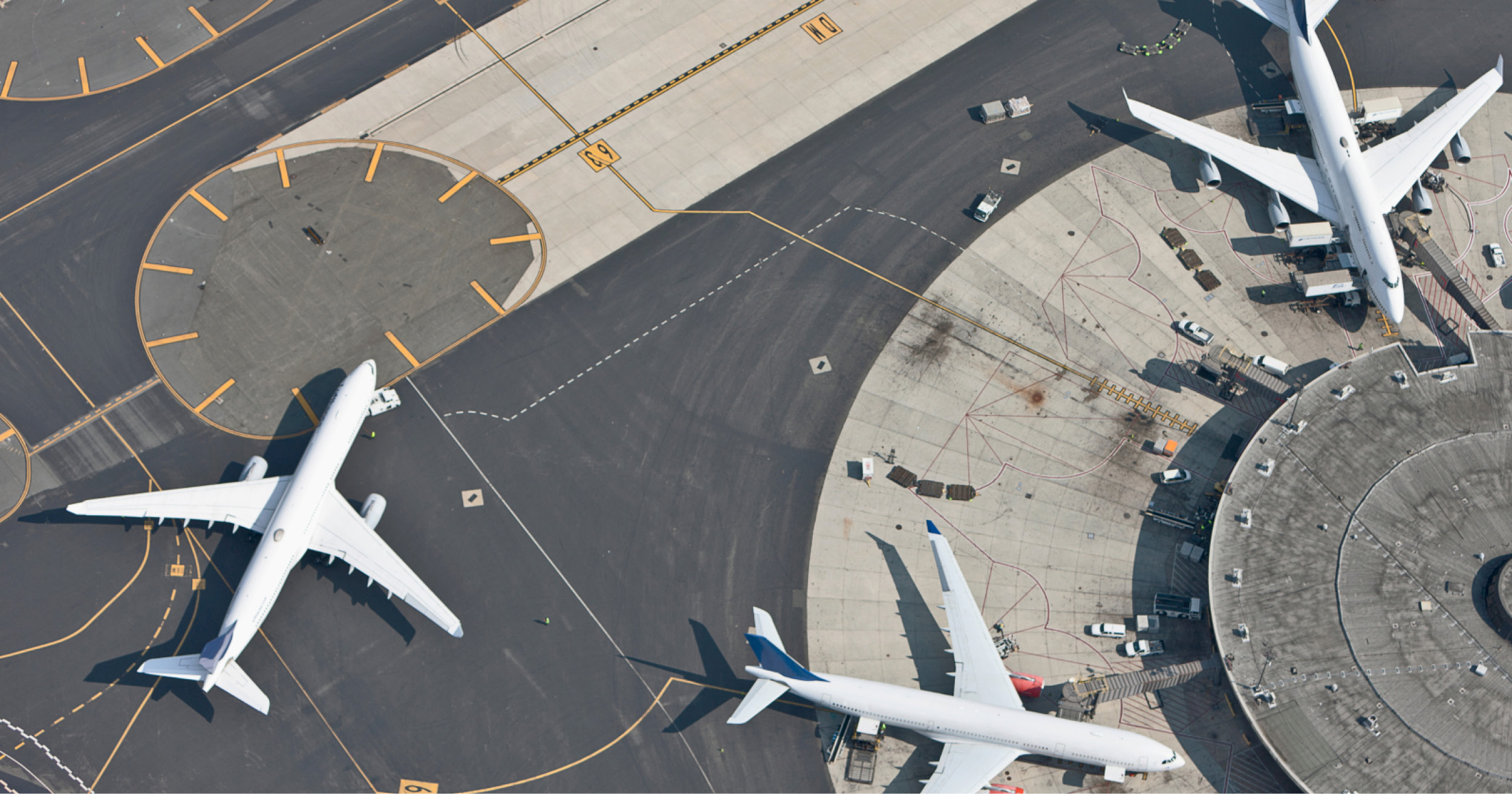 Overhead shot of two planes parked at airport gates and one plane taxiing